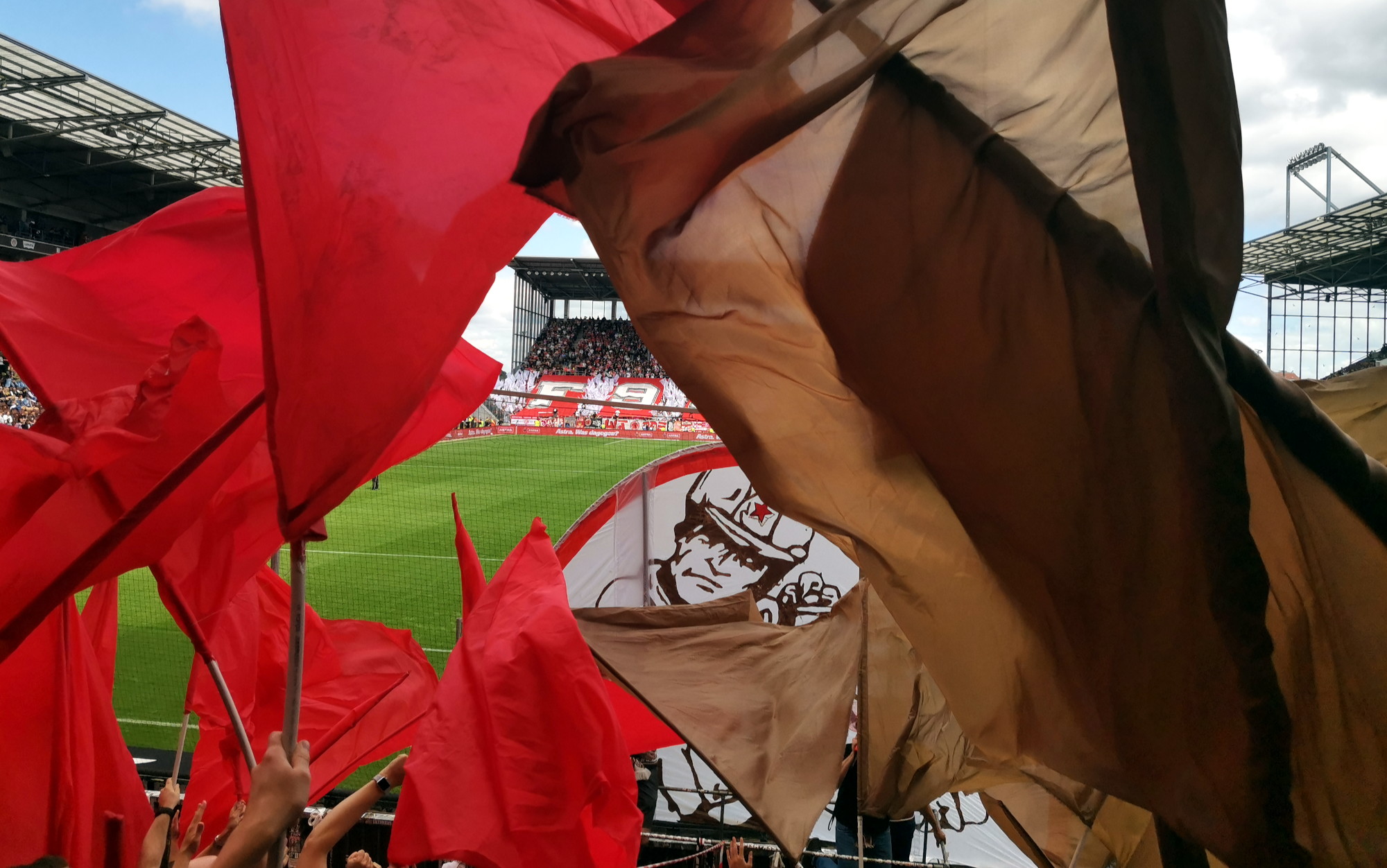 Zu sehen sind viele rote und braune Flaggen und ein Teil der Gästechoreo im Millerntor-Stadion beim 2. Saisonspiel vom FC St. Pauli gegen Fortuna Düsseldorf